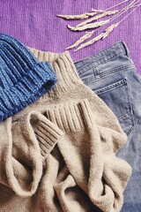 Blue wool hat, brown sweater and gray jeans on a purple background. Flat lay fall and winter fashion photography. Closeup detail clothes