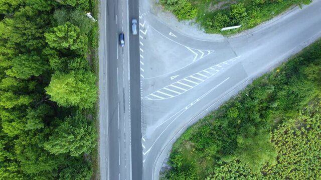 The movement of cars on the asphalt road between the greenery of trees, aerial view of the intersection of unequal roads