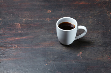 White cup with coffee on a dark wooden background, closeup. Tasty breakfast, morning routine concept