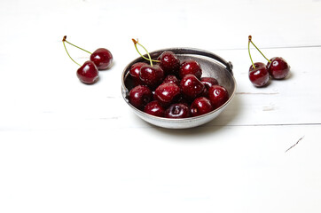 Sweet cherries in a metal bowl on wooden background, closeup. Fresh ripe sweet cherries in a bowl with droplets of water