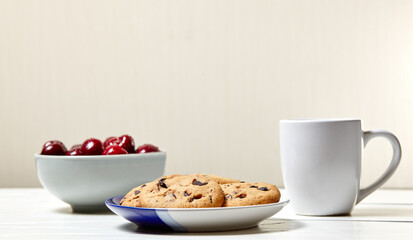 White cup with coffee, traditional cookies and sweet cherries in a ceramic bowl on a white wooden background, closeup. Tasty breakfast, morning routine concept