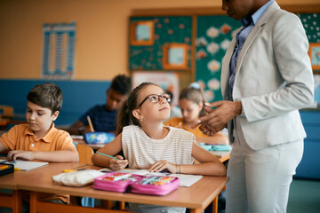 Fototapeta premium Little girl talks to her teacher while studying during class at elementary school.