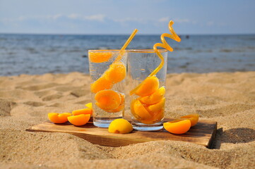 Peach cold drink with a straw on a sandy beach.