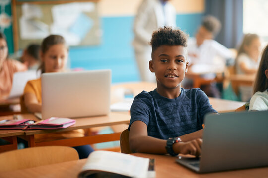 Smiling black elementary student uses laptop while e-learning during computer class at school.