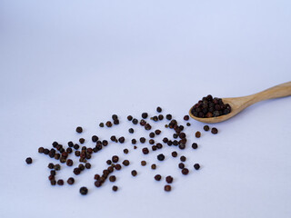 black pepper on wooden spoon and spread on ground with white background