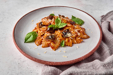Farfalle pasta with eggplant, tomato sauce, parmesan and basil on plate with napkin on gray background, close up. Selective focus