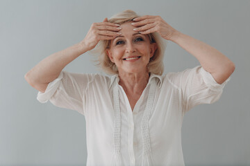 Elderly caucasian old aged woman gray haired portrait doing facebuilding yoga face gymnastics yoga self massage out wrinkles