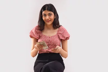 Fotobehang Portait of a young woman sitting and counting 500 rupees Indian currency notes. © IndiaPix