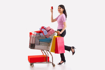 A young woman with credit card and colorful shoppingbags moving a cart full of gift boxes.