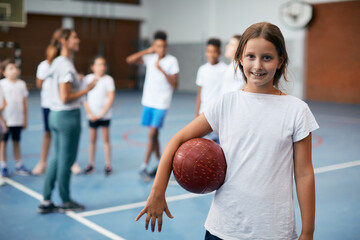 Happy girl holds volleyball ball during physical education class at school gym and looks at camera.