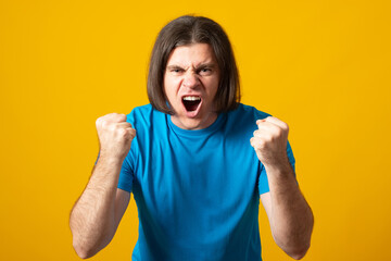 Young man wearing t-shirt standing over isolated yellow background crazy and mad shouting and yelling with aggressive expression and arms raised. Frustration concept.