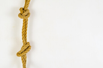 A natural rope with knots hangs against the white wall. Yellow r