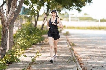 A healthy happy Asian woman runner in black sport outfits jogging in the natural city park under evening sunset