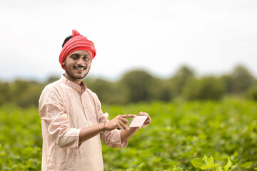 Indian farmer using smartphone at agriculture field.