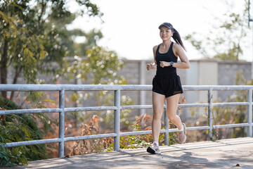 A healthy happy Asian woman runner in black sport outfits jogging in the natural city park under evening sunset