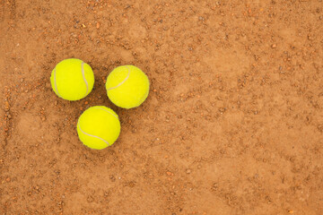 Yellow tennis balls lie side by side on a sandy court.