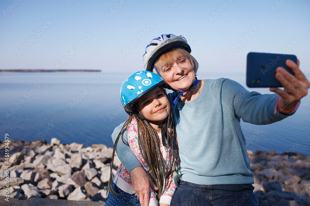 Wall mural Happy senior woman taking selfie together with grandchild after riding on roller skates, hugs and support, family activity, spring or fall outdoors, healthy lifestyle