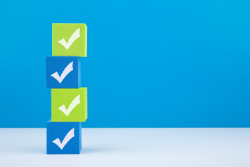 Four checkmarks on green and blue blocks on white table against blue background with copy space....