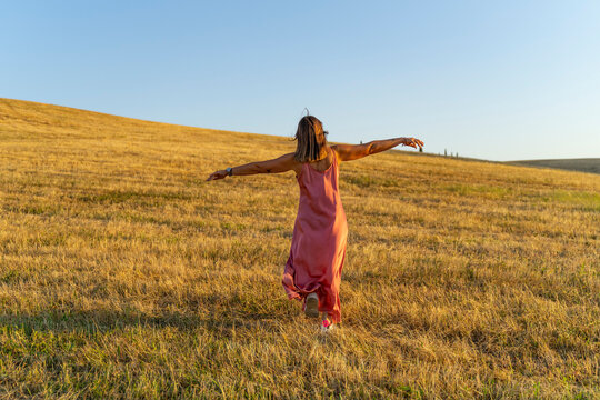 modella in posa a braccia aperte e vestito al vento in un campo di grano al tramonto