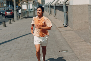Young indian woman sport runner jogging in wet sweaty t-shirt at city street.