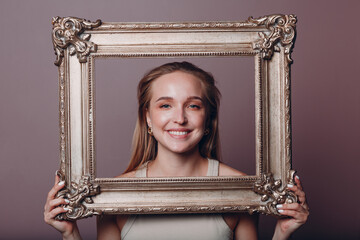 Millenial young woman blonde hair holds gilded picture frame in hands face portrait.