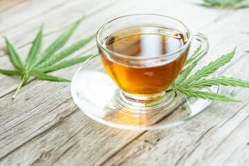 Glass cup of cannabis herbal tea. Cup of tea with marijuana and fresh green leaves on the wooden...