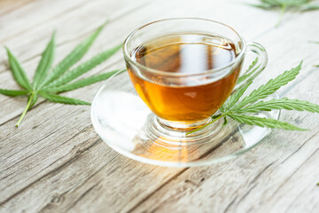 Glass cup of cannabis herbal tea. Cup of tea with marijuana and fresh green leaves on the wooden background.
