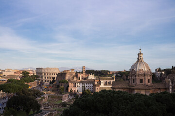 Fototapeta na wymiar View of Rome from the Capitoline hill.Behind the trees, the Church of Santa Maria Aracoeli, the Colosseum against the background of the city and the sky