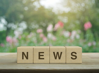 NEWS letter on block cubes on wooden table over blur pink flower and tree in garden, Business...
