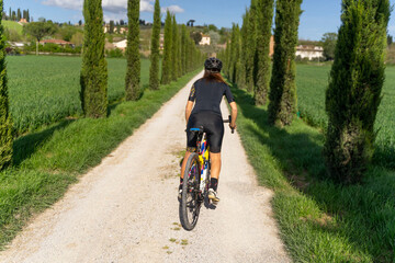 Naklejka premium ragazza pedala lungo un viale di cipressi in toscana sulla sua bicicletta Gravel
