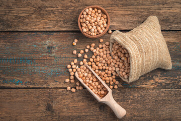 Raw chickpeas are poured out of a bag on a wooden table. Top view, copy space.