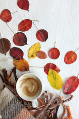 frothy coffee in a cup on a wooden table with red and yellow leaves and a plaid top view. warming atmosphere of an autumn morning