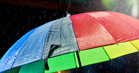 Umbrella in the colors of the rainbow during a rain shower