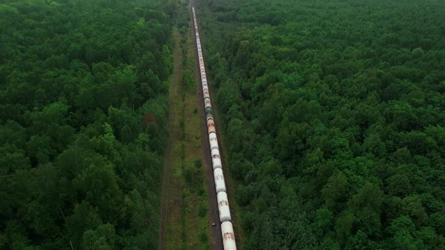 The train transports tanks of crude oil among virgin ecological green forests. Aerial view.