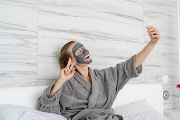 Woman with face mask relaxing sitting on the bed using mobile device