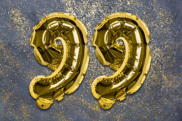 The number of the balloon made of golden foil, the number ninety-nine on a gray background with sequins. Birthday greeting card with inscription 99. Numerical digit, Celebration event, template.