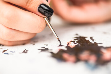 Home hobby - coloring picture by numbers, female hand with black manicure with brush, selective focus, close-up