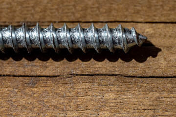 Macrophotography. Part of silver metal screw on brown wooden background. Copy space.