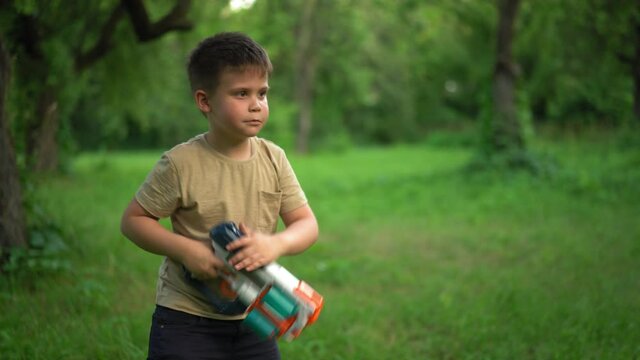 Child Holds Toy Gun and Shoots Cartridges. In Garden, Boy Laughs and Fires his Blaster. Kid is Playing Trendy Popular Blaster. Jule 2020. Kyiv, Ukraine. High quality 4k footage