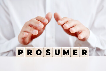 Business person holding his hands over the wooden cubes with the word prosumer. A person who...