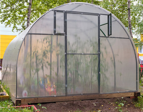 Handmade greenhouse from a metal framework and a polyethylene film on a farmer's land plot. Greenhouse Hotbed for vegetable seedlings.