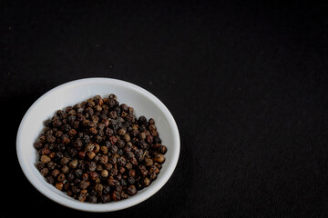 Fototapeta na wymiar Black Pepper isolated in a white bowl on a black background is used as an ingredient in Indian food. 