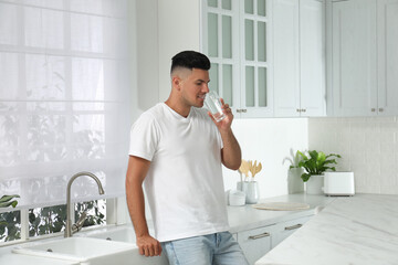 Man drinking tap water from glass in kitchen