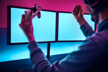 Man holding controller gesturing success in playing by rising hands. Blank monitor to insert your content.