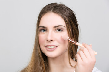 young woman is applying powder with a brush for everyday make up
