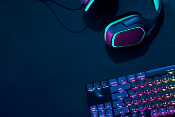 Headphones laying on desk next to rainbow colors backlighted gaming computer keyboard.