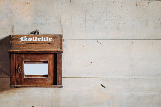 Holzkasten mit der deutschen Aufschrift "Kollekte", vor einer rauchen Wand in einer Kirche