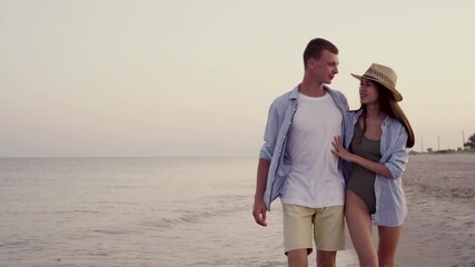 Happy married couple or lovers man and woman walk along the shore of the ocean or sea hug each other and kiss passionately on the beach. vacation concept at tropical resort.