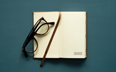 2022 calendar with space for text, notebook, brown bookmark, brown glasses, on a painted background, photo from above