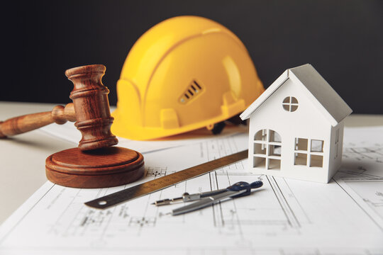 Judge gavel, white house and yellow hard hat with drawing tools on construction plan
